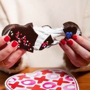 Woman's hands with red nail polish pulling apart a gooey marshmallow filled chocolate heart