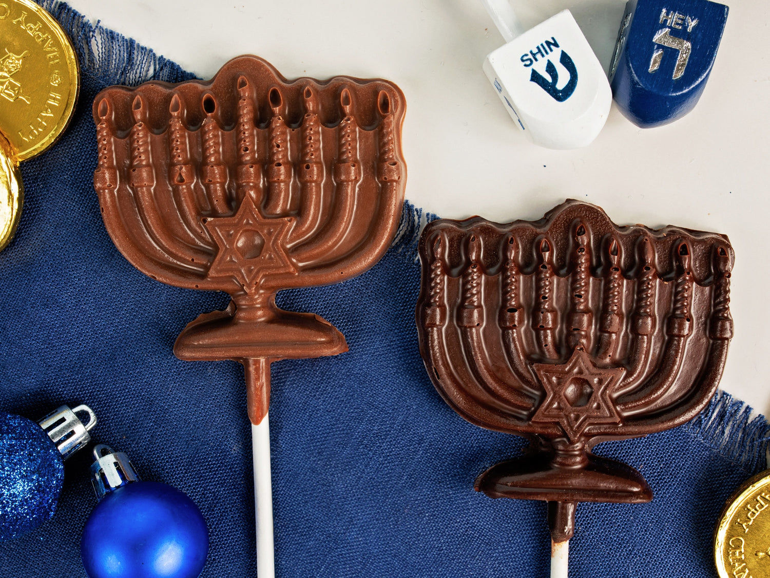 One milk chocolate and one dark chocolate dreidel on a table with other Chanukah decorations.