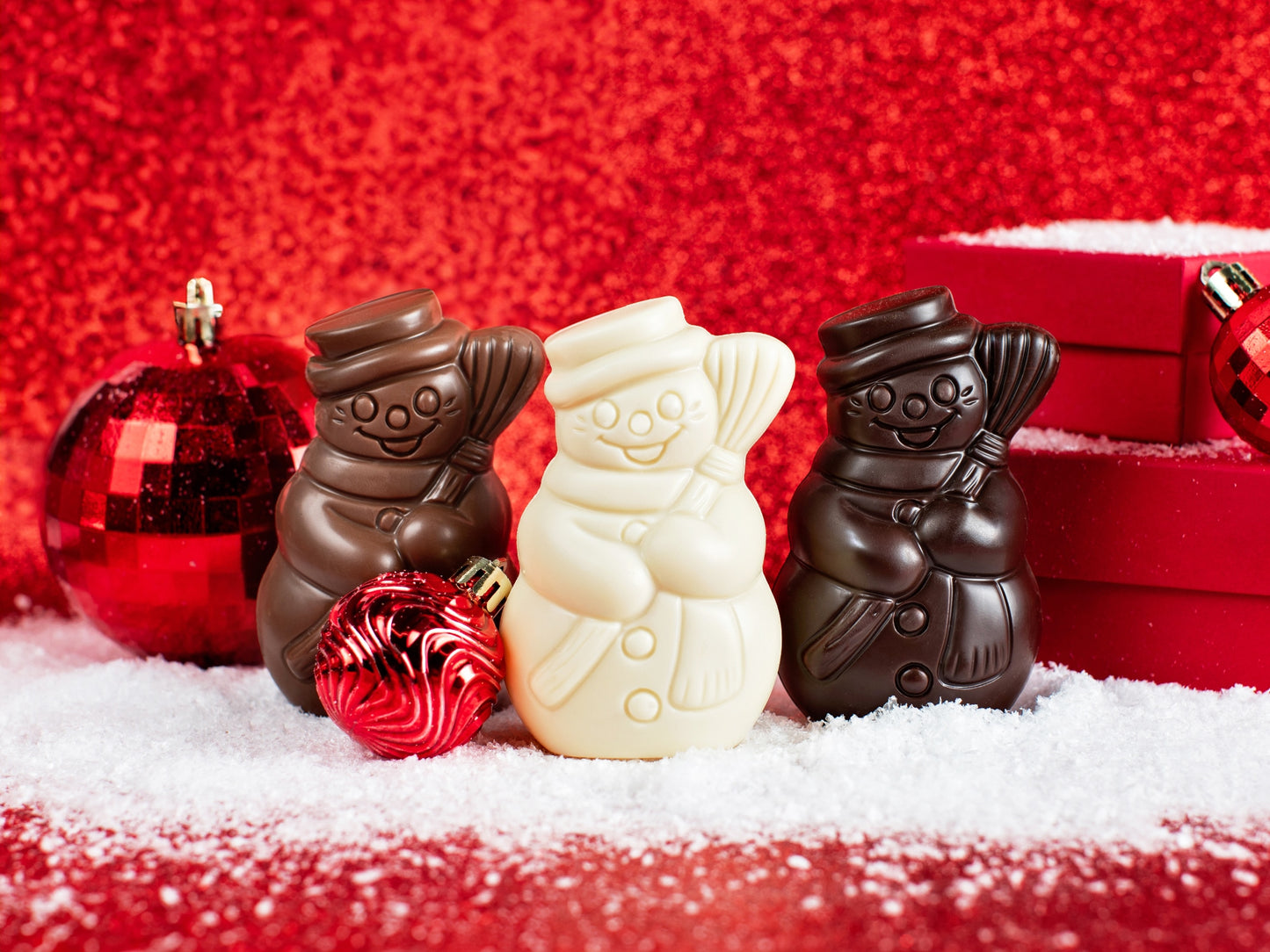 three small molded chocolate snowmen wearing top hats and carrying a broom.