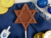 A milk chocolate star pop on a table with other Chanukah decorations.