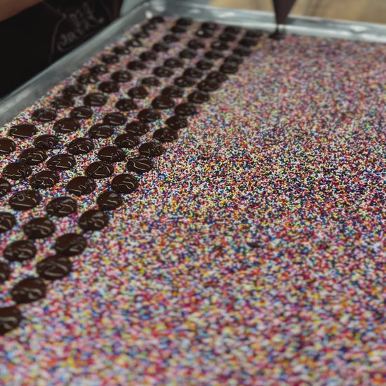 chocolate drops from a funnel onto a bed of nonpareil seeds