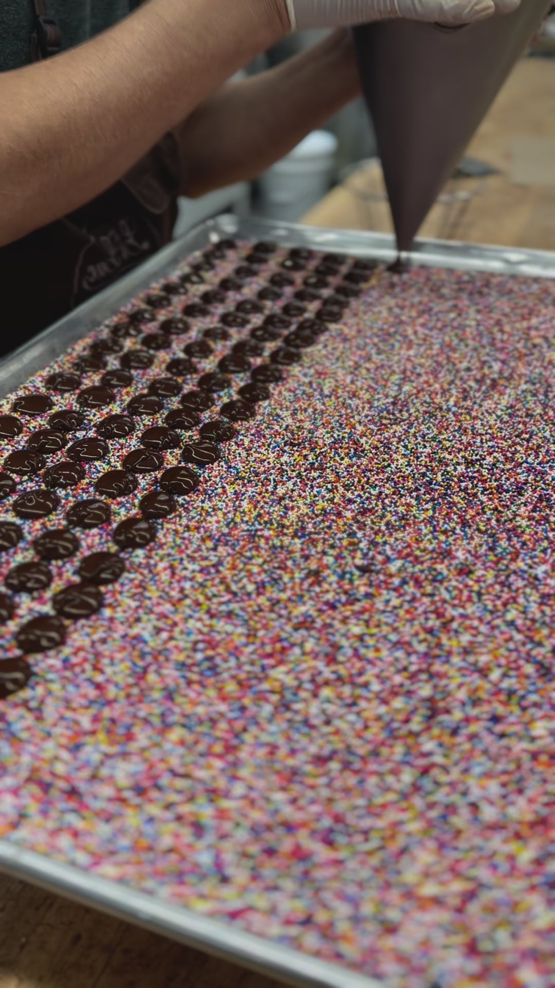 chocolate drops from a funnel onto a bed of nonpareil seeds