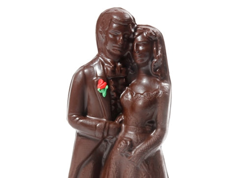 Three-dimensional molded chocolate Bride and Groom stand together with their arms entwined.