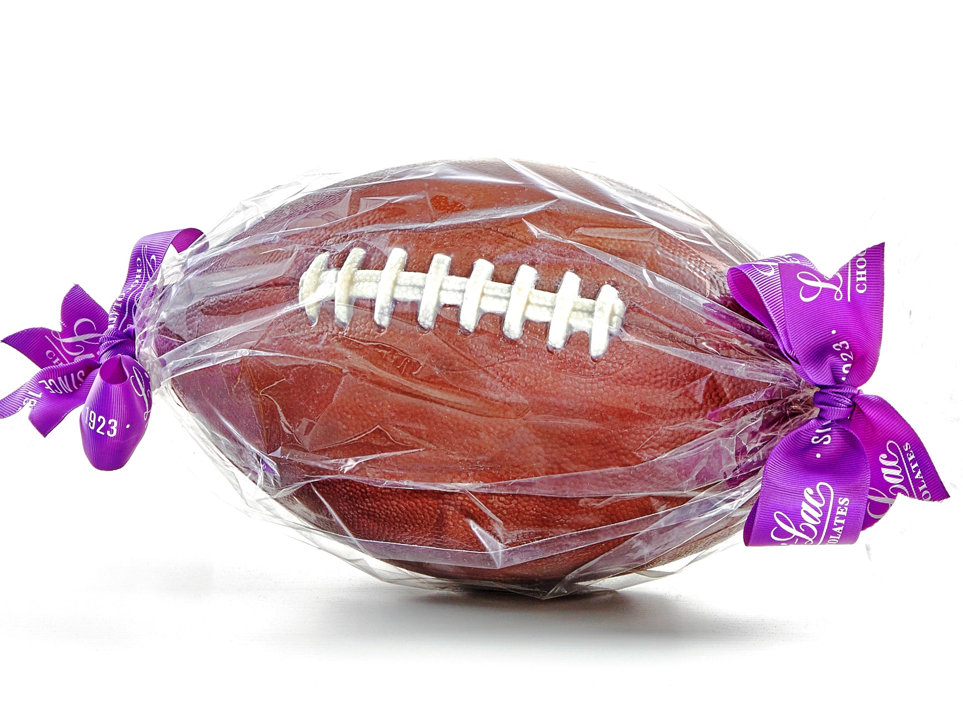 Life size molded chocolate football has pigskin texture and white chocolate laces stitching details. It is wrapped in clear cellophane and tied at each end with a tribbon.