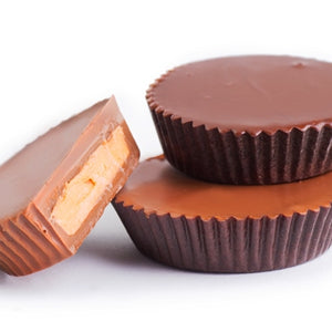 Milk and dark chocolate peanut butter cups are stacked together. One has been cut in half to reveal the creamy peanut butter center sandwiched between the top and bottom of chocolate in the cup.