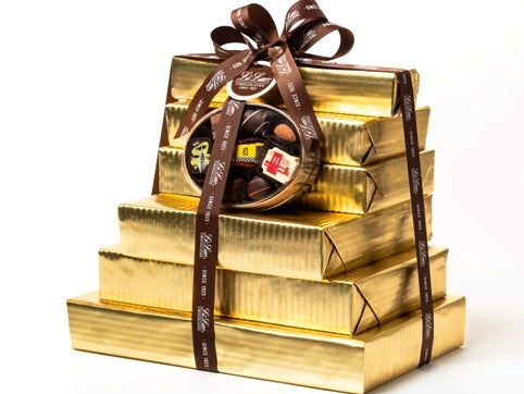 Nine boxes of chocolate have been beautifully gift wrapped in gold foil paper. They are stacked on top of each other and tied together with a dark brown Li-Lac Chocolates logo printed ribbon with a round gift tag.