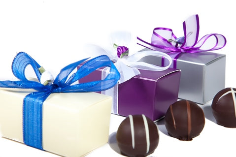 Three assorted gourmet chocolate ganache truffles sit next to three small rectangular cardstock boxes in different colors. The boxes are tied with different colored ribbon bow. 